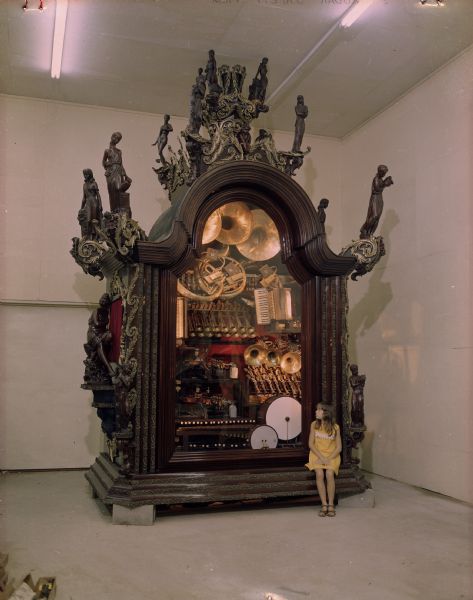 Large glass fronted case filled with instruments. A young girl is sitting on the front of the case which is in the main house. One of several photographs used in a brochure for House on the Rock. 