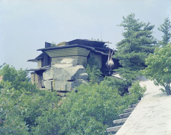 Elevated view of House on the Rock. Some of the view is obscured by trees growing in and around the roof of the walkway.