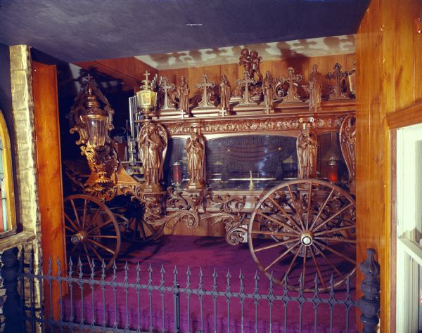 The Pontalba Hearse, made of carved wood displayed behind a fence. This image was used in the original brochure for the House on the Rock. 
