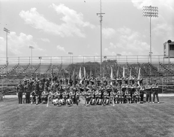 Outdoor group portrait of the Madison Drum and Bugle Corps in uniform. The group is posing on the field at Warner Park with bleachers in the background.
