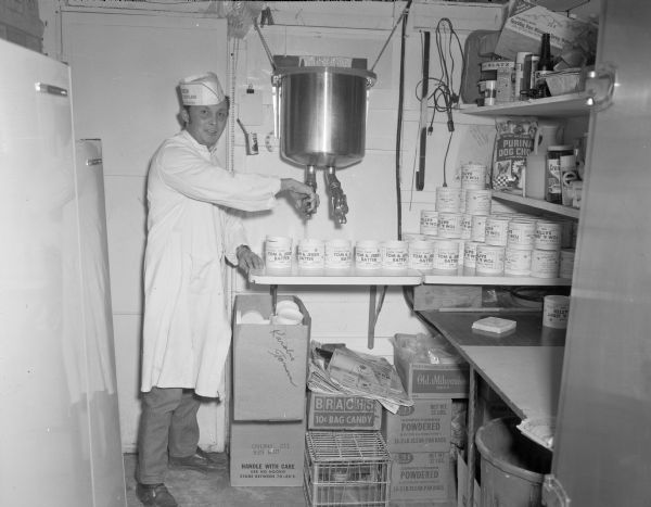 A Karabis Tavern employee wearing a paper hat and white coat fills Tom & Jerry batter containers in a kitchen or preparation area. 