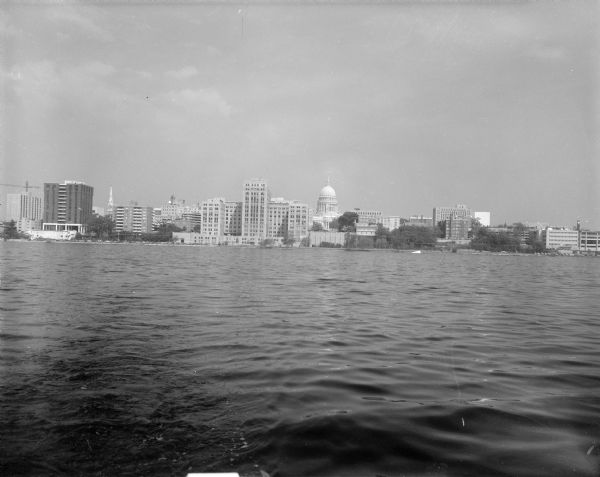 View across Lake Monona looking north towards the Madison skyline. In the foreground is what appears to be the back of a boat and a wake in the water.
