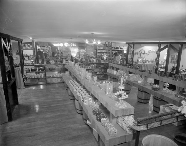 Elevated interior view of Del Wood's Country Store. Items are on display on open shelves, and on shelves set up on barrels. Two people are standing in the background on the right.