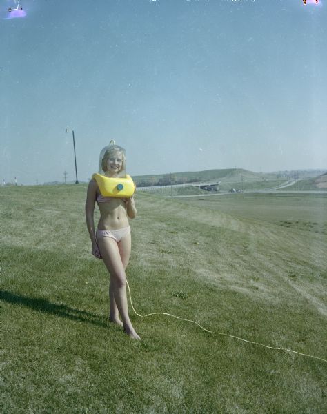 Faye Geise, wearing a bikini, is standing and posing with the Aqua Form on her head.  