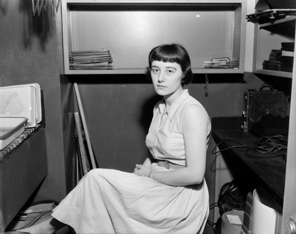 Portrait of Bea Walusiak Heitmeyer wearing a dress and sitting in the darkroom. 