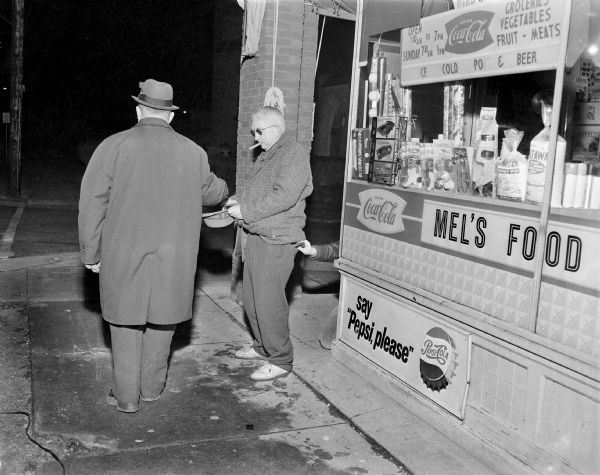 NEW:
Sid is standing outside of Mel's Food, begging with his hat in his hands. Sid is wearing sunglasses and has a cigar in his mouth. The back of a passerby, who is wearing an overcoat and a hat, appears to be dropping money into Sid's outstretched hat. On the right a man is stooping (only his arm and knee are visible) behind the corner of the storefront and pulling out what may be Sid's wallet from his back pocket.