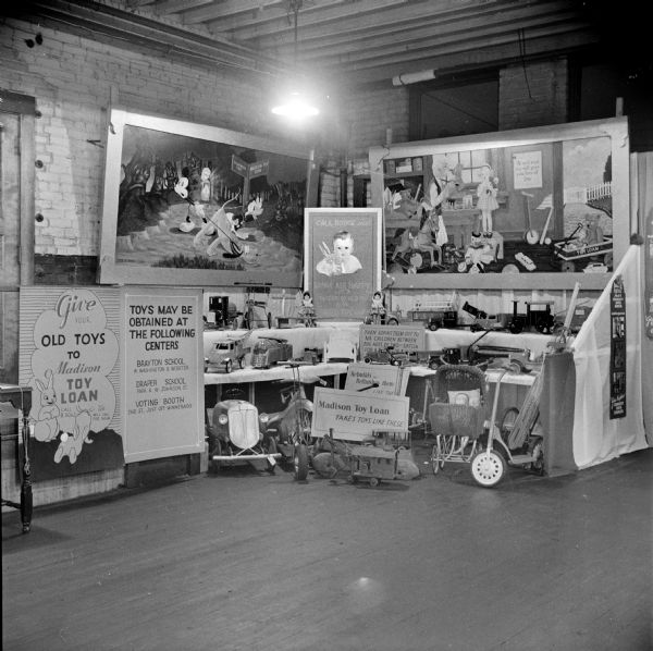 Display for the Madison Toy Loan program, set up in the corner of an industrial building. Signs for the display read: "Madison Toy Loan takes toys, like these. Rebuilds and refurnishes them, like these. Then loans them out to all children between the ages of two and sixteen . . ." A sign on the left reads: "Toys may be obtained at the following centers: Brayton School, W. Washington & Webster, Draper School, Park & W. Johnson St., voting booth, 2nd St. just off of Winnebago." There are two large paintings, and the one on the left has Disney characters. The toys on display on the floor and on shelves are in various states of repair. Sid worked on the painting in the back right (Image ID: 122762).
The 1940 census lists Sid Boyum as an artist/government worker for the Toy Loan Program, which was started by the Works Progress Administration (WPA) in the spring of 1940.