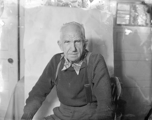 An older Sid posing for a portrait. He is wearing a sweater and suspenders.