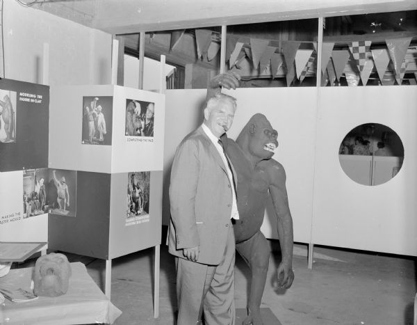 Sid posing with a clay model of Sambo, one of the Milwaukee County Zoo's gorillas during the 1950s. Sid is wearing a suit and has a cigar in his mouth. Behind him is a display of the making of the model of Sambo.