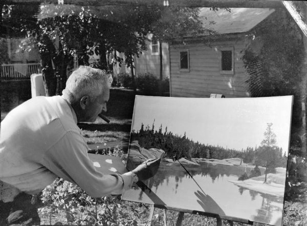 Sid Boyum, standing in his backyard, painting a landscape depicting Little Fork River in northwest Minnesota.