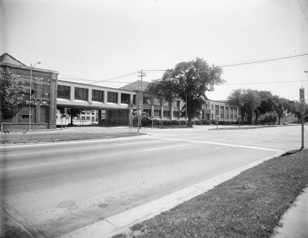 View across East Washington Avenue towards the Gisholt factory at the intersection of Baldwin Street. There is an enclosed skybridge (called an "overhead" at the time of the industrial expansion approval in 1966) that connects the factory buildings across Baldwin Street.