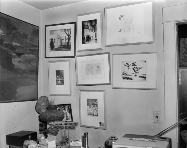 View of interior of Sid's office with a number of paintings and other artworks framed and displayed on a wall in the corner of a room above a table with lamps and a television.