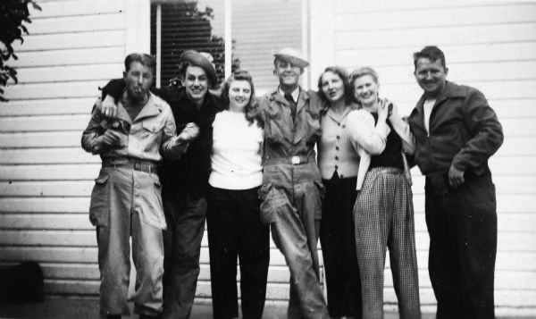 Group portrait of Sid and his sister Bernice standing with three other men and two women in front of a white clapboard house. Two of the men are wearing military-style coveralls.