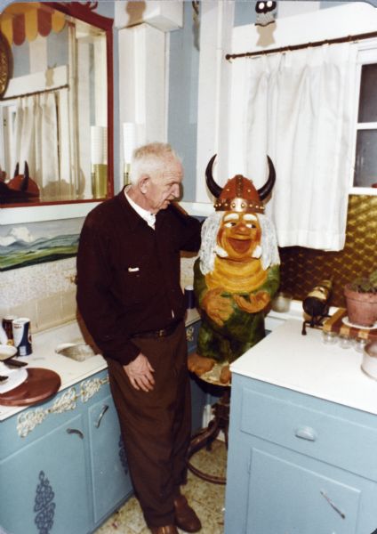 Sid standing in his kitchen looking at a sculpture of a Viking troll set up on a stool.