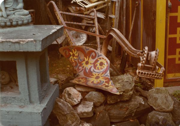 Hand-painted plow, with design of flowers in Sid's backyard, next to the Tea House and the base of a sculpture.