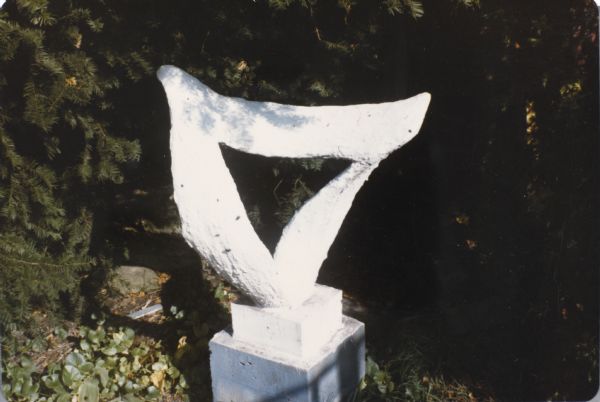 Small, white, triangular abstract form on square two-tiered base in Sid's backyard.