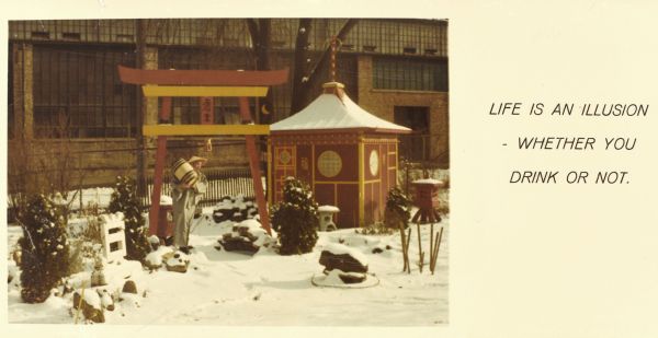 Christmas card by Sid of himself standing in his backyard in the tea garden. Boyum, in grey kimono and straw conical hat and holding a small wooden keg, is standing under the torii gate, amid small lanterns near the tea house. Snow is on the ground. Madison-Kipp Corporation is in the background. Text on card reads: "Life is an illusion whether you drink or not."