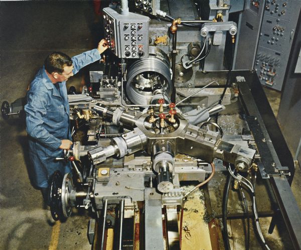 Color illustration art of an overhead view of a man operating a Number 5 Ram Turret machine with a control panel. Metal shavings are scattered on the machine. The machine is flat with six arms extending from a center.