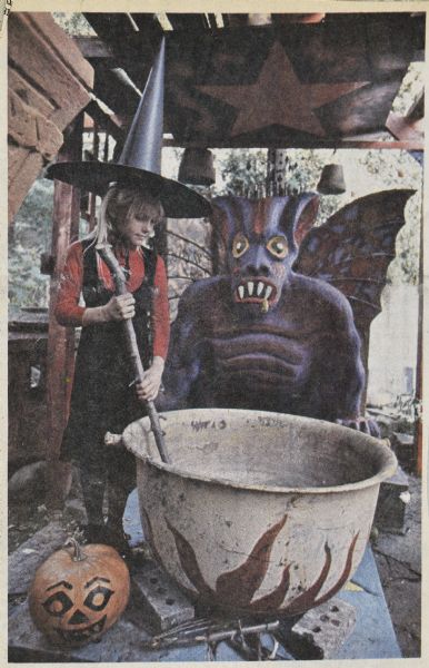 Newspaper (<i>Capital Times</i>) photograph of Sid Boyum's neighbor Johanna Oosterwky wearing a witch's hat and stirring a cauldron in front of the Devil sculpture in Sid Boyum's backyard. There is a painted pumpkin Jack-o-lantern in the foreground.