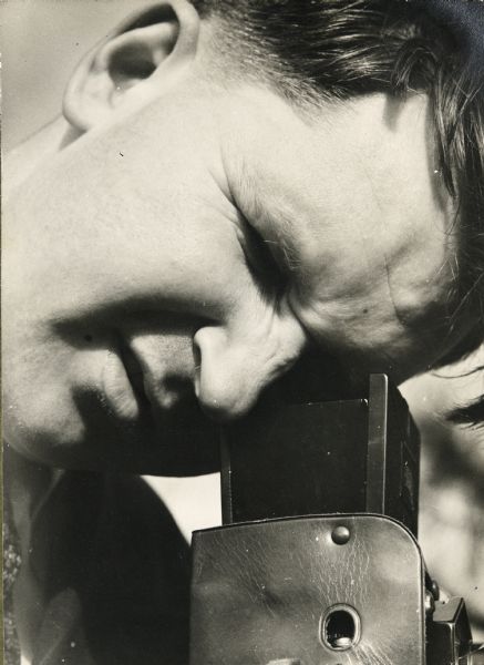 Close-up of Sid looking through the viewfinder of a twin-lens reflex. 