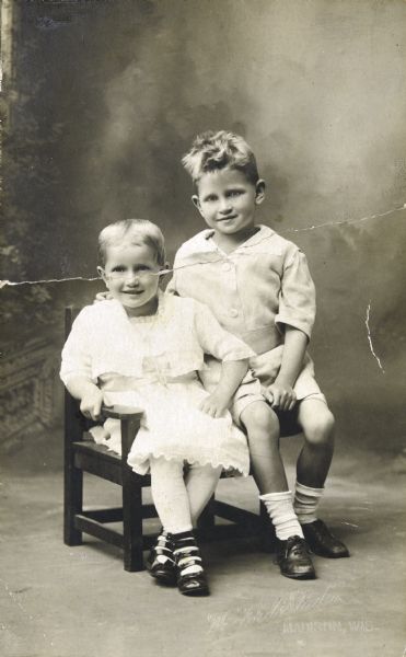 Studio portrait in front of a painted backdrop of Sid (right) and his younger sister, Bernice (left). 