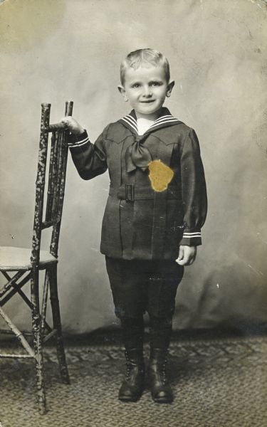 Full-length portrait of John Boyum, Sid's brother, standing near a chair. 