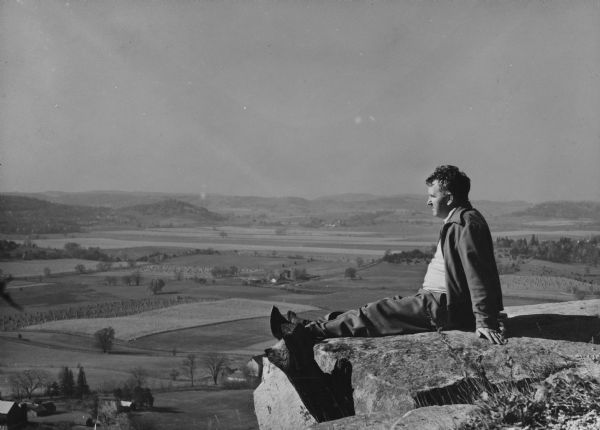 Photo collage of Sid sitting on the edge of a rocky overlook. Fields and hills are in the valley below.