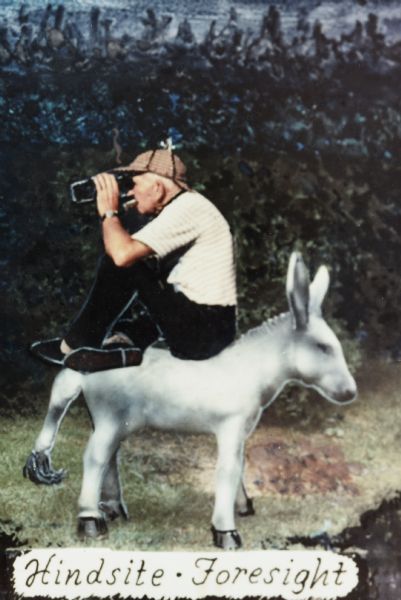 Sid sitting backwards on a donkey, with a cigar in his mouth and wearing a hat. He is looking through what appears to be a pair of binoculars. Caption at the bottom reads: "Hindsite, Foresight."