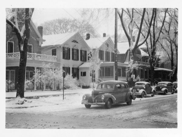 View looking north across intersection towards the 400 block of North Carroll Street. A light snow clings to the trees and roofs of the houses. A car is approaching Gorham Street in the foreground; other cars are parked along the curb.