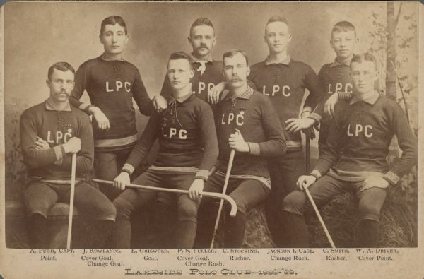 Studio cabinet card group portrait in front of a painted backdrop of the eight members of the Lakeside Polo Club of Racine. Four members are standing behind the others, who are sitting on studio props. The men wear athletic uniforms, and five of them are holding "canes" or modified hockey sticks. They are identified as (left to right): A. [Arthur] Pugh, Capt. Point; J. Rowlands, Cover Goal, Change Goal; E. Grisold, Goal; P.S. Fuller, Cover Goal, Change Rush; C. Stocking, Rusher; Jackson I. Case [son of Jerome I. Case, founder of J.I. Case Threshing Machine Company], Change Rush; C. Smith, Rusher; W.A. Driver, Cover Point. Pugh, Griswold and Stocking are each wearing a medal pinned to his jersey. "Polo" in this case refers to roller hockey, played indoors on roller skates. 