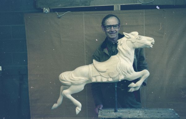 Portrait of a man standing behind a horse sculpture. 