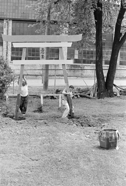 Sid and a man are struggling to set the torii gate upright in Sid's backyard. 