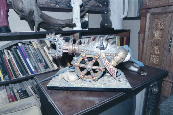 Sculpture of a cannon in the shape of an imaginary dragon on top of a television set in Sid's living room. Behind the sculpture is a bookcase full of books and other objects.