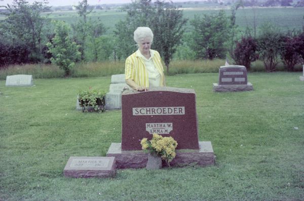 Outdoor portrait of Bernice (Boyum) Bergner standing behind a gravestone for her aunt Martha W. and her mother Emma M. Schroeder Boyum in the Hillside Cemetery in Columbus, Wisconsin. Martha died in 1963 and Emma in 1974. Photo taken after Emma's funeral.