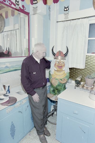 Sid is standing in his kitchen looking at a sculpture of a Viking troll set up on a stool.
