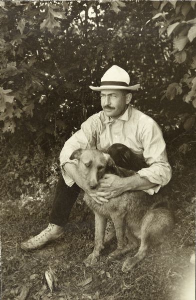 Bill Marr sitting on the ground outdoors with his arms around Carl's Airedale dog, Diadem (Di).