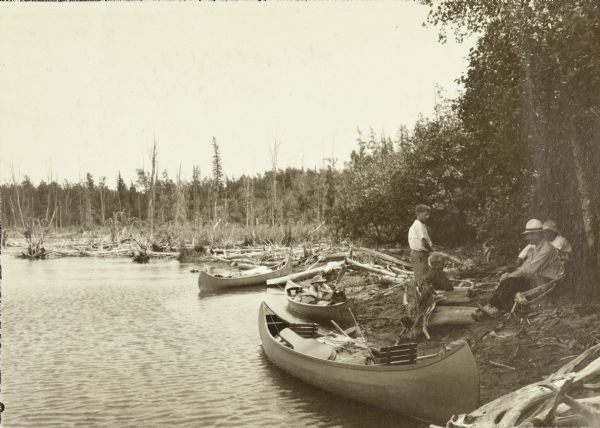 View down shoreline towards the travelers pausing in their canoe journey to have lunch on the riverbank below Gordon Dam. 