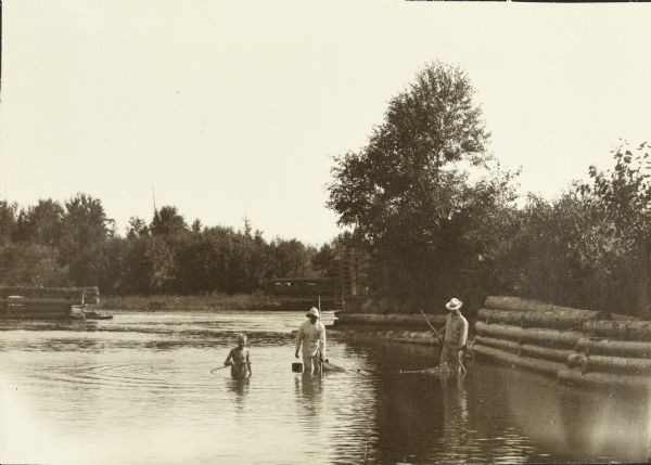View across water towards Carl Greene, Dr. Ernest Copeland ("Doc" or "Cope"), and Bill Marr wading in the river, seining for minnows.