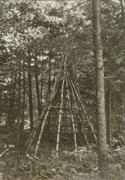 The wooden frame of an Indian tipi (teepee) among trees in the woods.