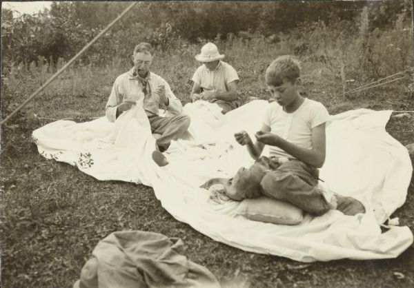 Howard Greene (left), another traveler (middle), and young Howard T. Greene are improvising and sewing a needed tent fly while in camp.