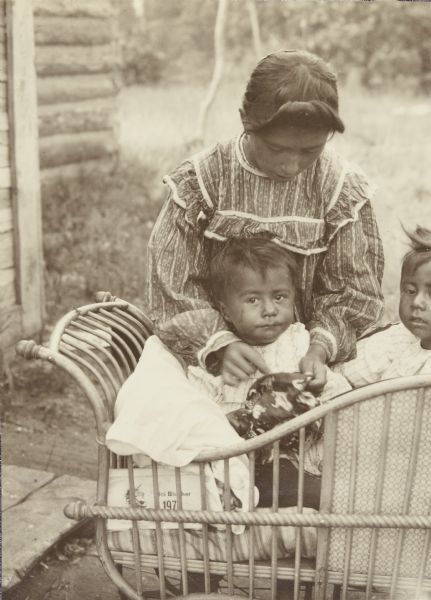 A woman tending to two babies who are sitting in an ornate crib outdoors.