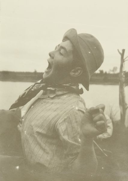 Close-up of Clay stretching and yawning. He is wearing a hat, and the St. Croix River is in the background.