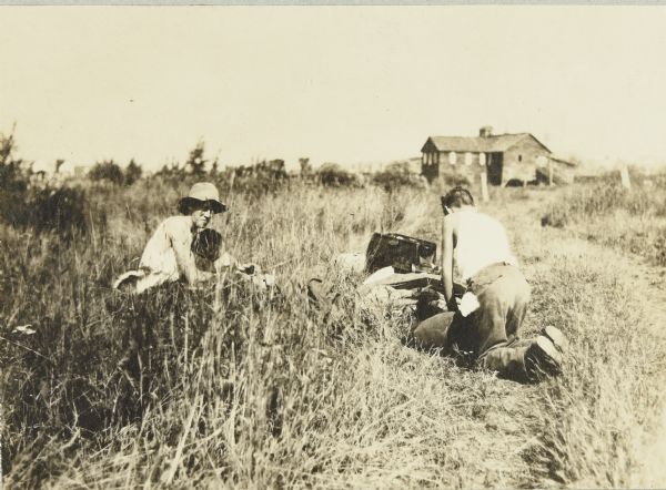 Two of the men, in a field near Glidden, Wisconsin, loading their packs in preparation for the canoe trip. There is a house in the background.