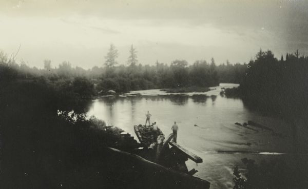 A view of Bear Lake and the surrounding forested area. Several of The Gang are standing on a dam.