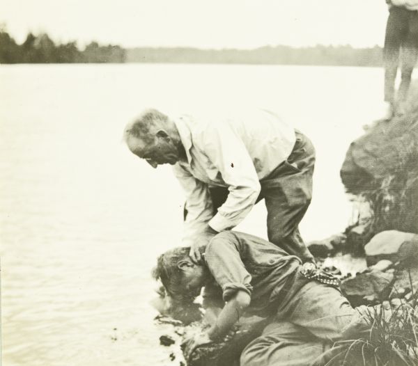 Doc Copeland helps Jack wash off the toothpaste by dipping Jack's face in the Chippewa River.