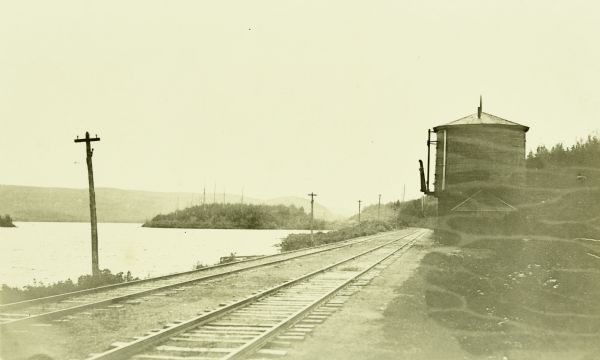 A view down railroad tracks toward a water tank. Lake Windigoostigwan is on the left.