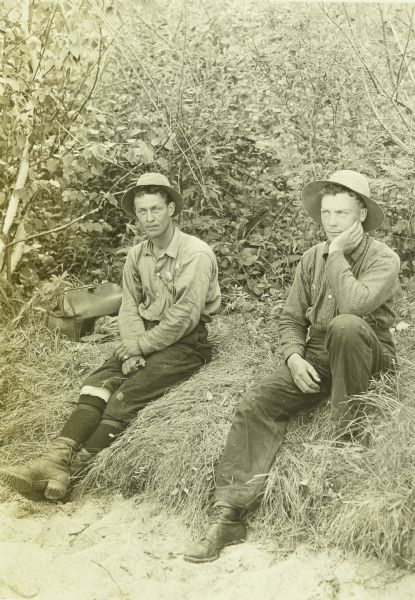 Two Canadian rangers sitting on the grass. They are wearing hats and leather boots. 