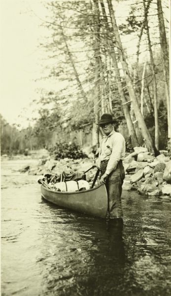 One of The Gang standing in shallow water next to a canoe which is loaded with supplies.