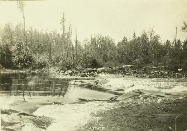 Rapids on the Namakan River, featuring an apron of smooth water and a rocky shoreline on the opposite side.