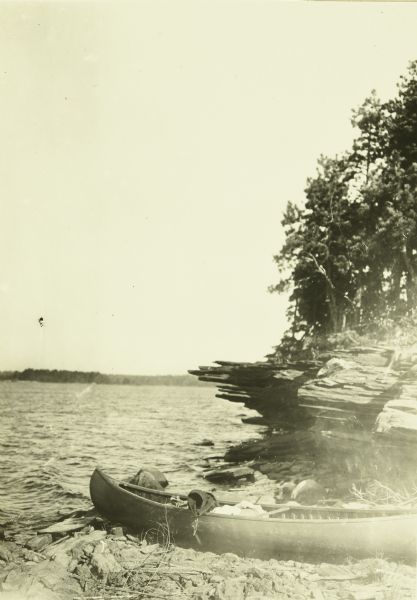 A canoe is on the rocky shore near an outcrop. 